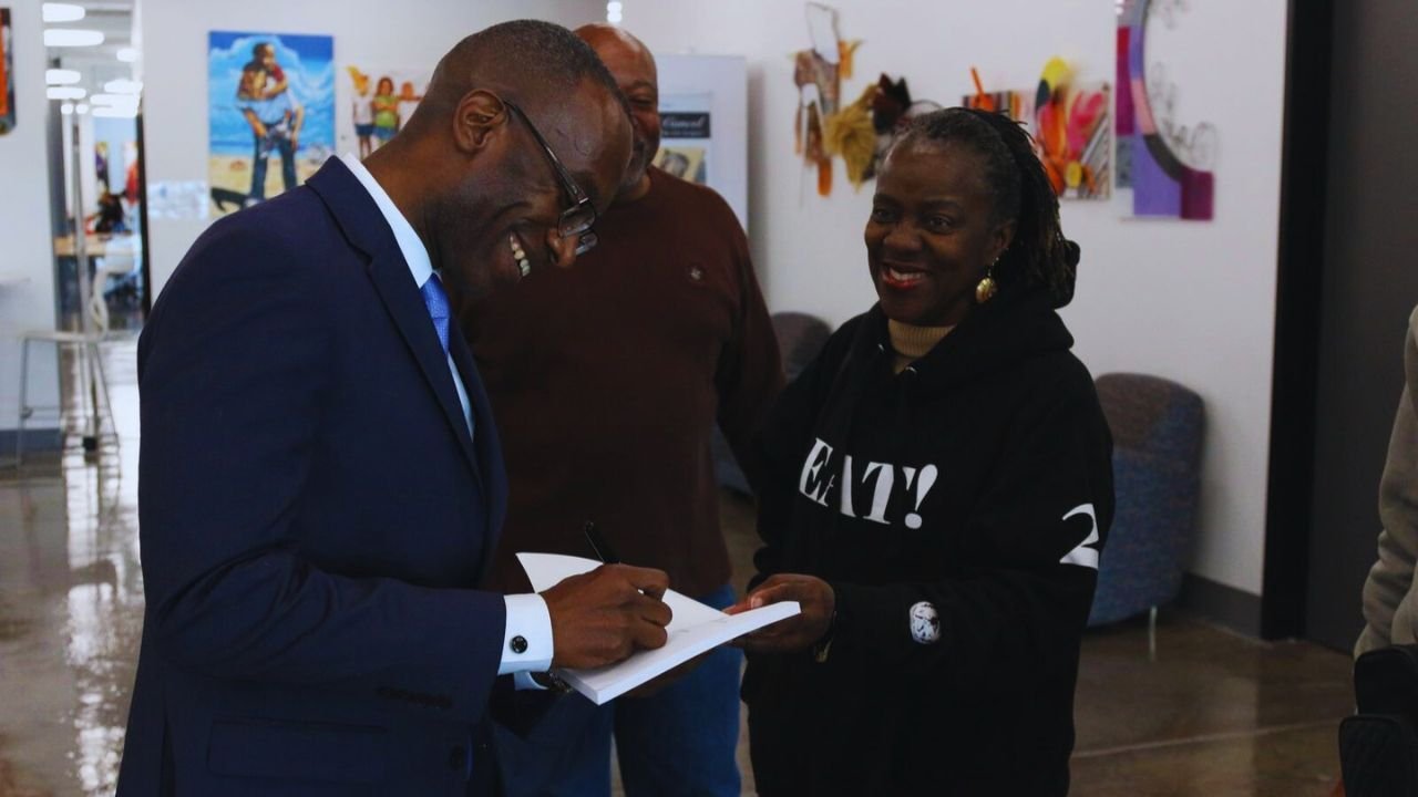 Dr. Michael Thompson smiling as he receives a book to sign from someone.
